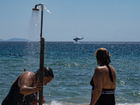 Bathers are enjoying the sea while a firefighting helicopter is collecting water from it in Nea Makri, Greece, on August 14, 2024, as it is...