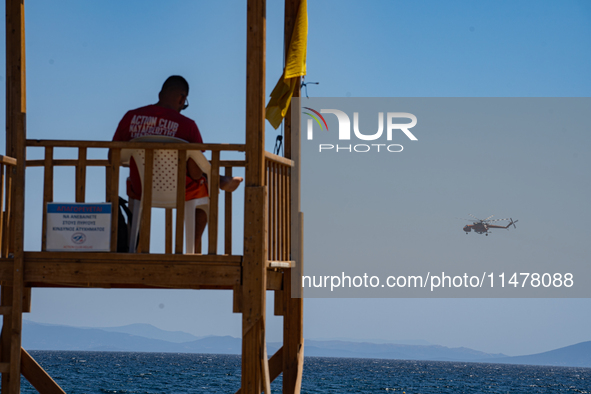 A lifeguard is sitting in the tower while a firefighting helicopter is collecting water from the sea in Nea Makri, Greece, on August 14, 202...