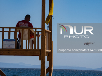 A lifeguard is sitting in the tower while a firefighting helicopter is collecting water from the sea in Nea Makri, Greece, on August 14, 202...