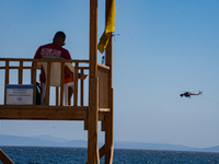 A lifeguard is sitting in the tower while a firefighting helicopter is collecting water from the sea in Nea Makri, Greece, on August 14, 202...