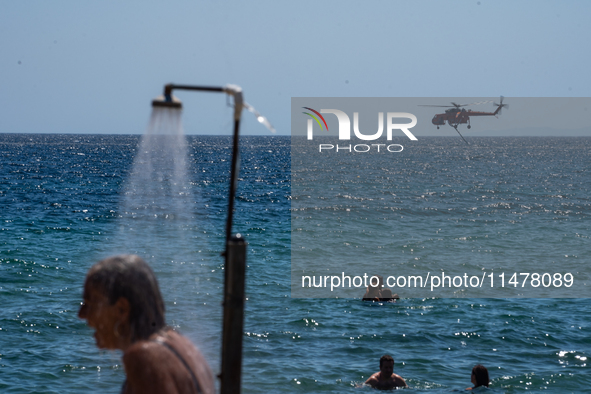 Bathers are enjoying the sea while a firefighting helicopter is collecting water from it in Nea Makri, Greece, on August 14, 2024, as it is...