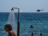 Bathers are enjoying the sea while a firefighting helicopter is collecting water from it in Nea Makri, Greece, on August 14, 2024, as it is...