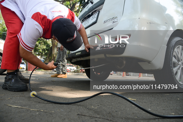 An officer is testing a probe in the exhaust pipe of a vehicle as part of an exhaust emissions test in Bogor, West Java, Indonesia, on Augus...