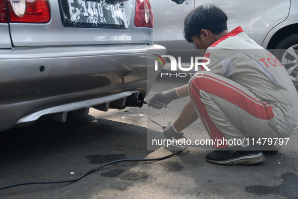 An officer is testing a probe in the exhaust pipe of a vehicle as part of an exhaust emissions test in Bogor, West Java, Indonesia, on Augus...