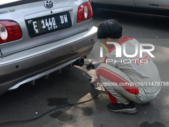 An officer is testing a probe in the exhaust pipe of a vehicle as part of an exhaust emissions test in Bogor, West Java, Indonesia, on Augus...