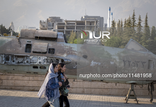 Two young Iranian women are walking past an Iraqi crashed fighter jet at the War Museum at a park in central Tehran, Iran, on August 15, 202...