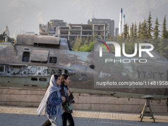 Two young Iranian women are walking past an Iraqi crashed fighter jet at the War Museum at a park in central Tehran, Iran, on August 15, 202...