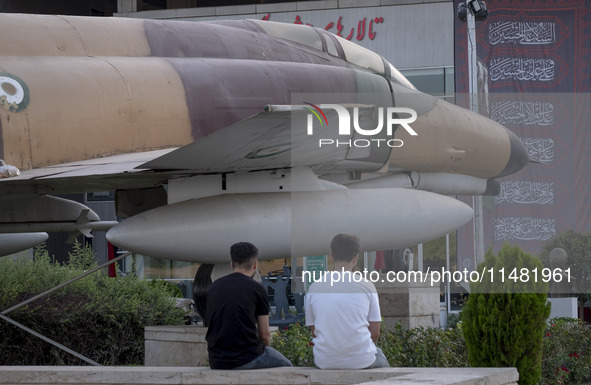 Two young Iranian men are sitting together under an Iranian F-4 fighter jet that is placed at the War Museum at a park in central Tehran, Ir...