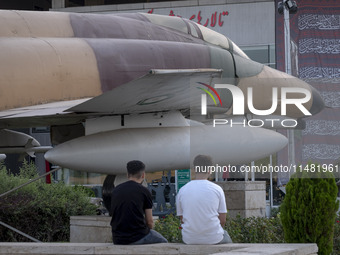 Two young Iranian men are sitting together under an Iranian F-4 fighter jet that is placed at the War Museum at a park in central Tehran, Ir...