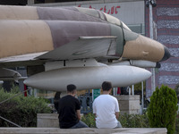 Two young Iranian men are sitting together under an Iranian F-4 fighter jet that is placed at the War Museum at a park in central Tehran, Ir...