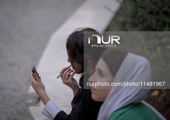 A young Iranian woman is putting on makeup while sitting at a park in central Tehran, Iran, on August 15, 2024. 