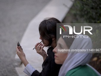 A young Iranian woman is putting on makeup while sitting at a park in central Tehran, Iran, on August 15, 2024. (