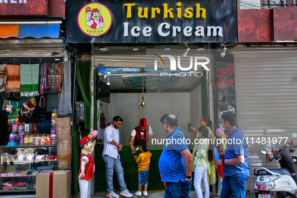 A Turkish ice cream vendor is performing tricks as he entertains a young boy along the Mall Road in Mussoorie, Uttarakhand, India, on April...