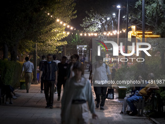 Iranian people are walking along a sidewalk at a park in central Tehran, Iran, on August 15, 2024. (