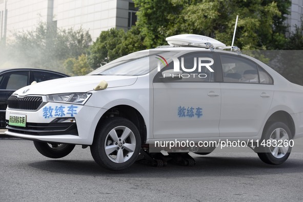 A firefighting robot is spraying water under the chassis of an electric vehicle that is simulated to be on fire and is lifting the vehicle t...