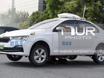 A firefighting robot is spraying water under the chassis of an electric vehicle that is simulated to be on fire and is lifting the vehicle t...