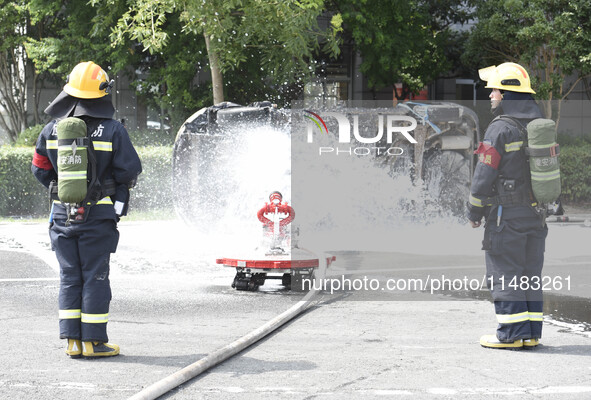 A firefighting robot is spraying water under the chassis of an electric vehicle that is simulated to be on fire and is lifting the vehicle t...