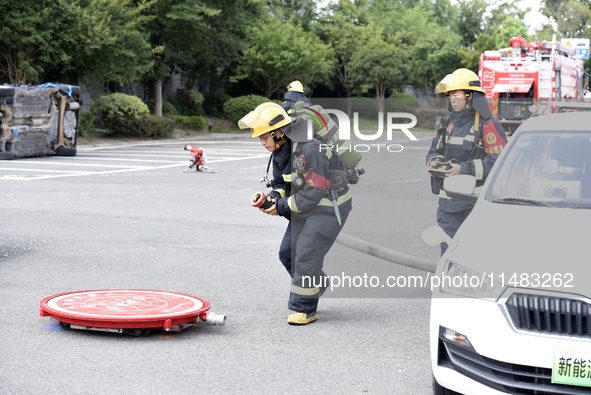 A firefighting robot is spraying water under the chassis of an electric vehicle that is simulated to be on fire and is lifting the vehicle t...