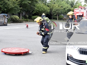 A firefighting robot is spraying water under the chassis of an electric vehicle that is simulated to be on fire and is lifting the vehicle t...