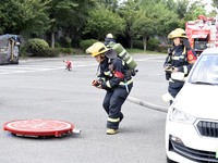 A firefighting robot is spraying water under the chassis of an electric vehicle that is simulated to be on fire and is lifting the vehicle t...