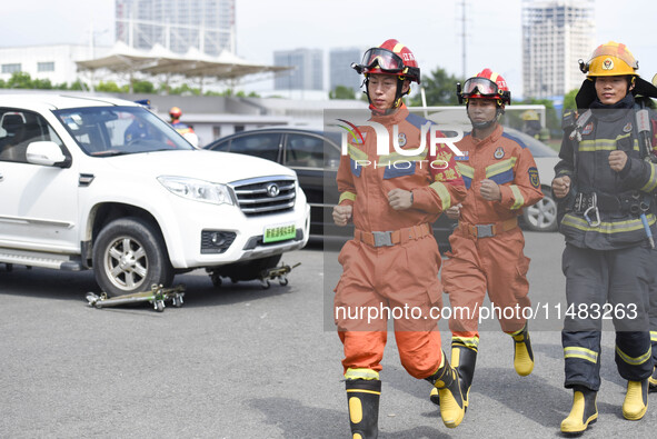 A firefighting robot is spraying water under the chassis of an electric vehicle that is simulated to be on fire and is lifting the vehicle t...