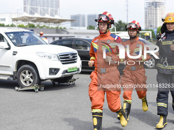 A firefighting robot is spraying water under the chassis of an electric vehicle that is simulated to be on fire and is lifting the vehicle t...