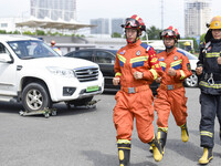 A firefighting robot is spraying water under the chassis of an electric vehicle that is simulated to be on fire and is lifting the vehicle t...