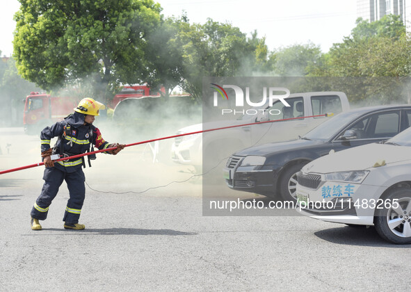 A firefighting robot is spraying water under the chassis of an electric vehicle that is simulated to be on fire and is lifting the vehicle t...