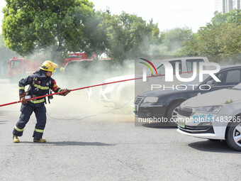 A firefighting robot is spraying water under the chassis of an electric vehicle that is simulated to be on fire and is lifting the vehicle t...