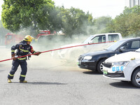 A firefighting robot is spraying water under the chassis of an electric vehicle that is simulated to be on fire and is lifting the vehicle t...