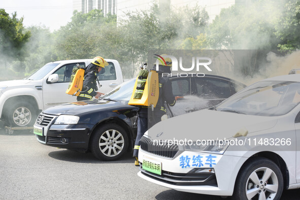 A firefighting robot is spraying water under the chassis of an electric vehicle that is simulated to be on fire and is lifting the vehicle t...