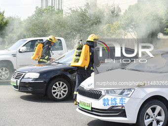 A firefighting robot is spraying water under the chassis of an electric vehicle that is simulated to be on fire and is lifting the vehicle t...