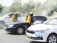 A firefighting robot is spraying water under the chassis of an electric vehicle that is simulated to be on fire and is lifting the vehicle t...