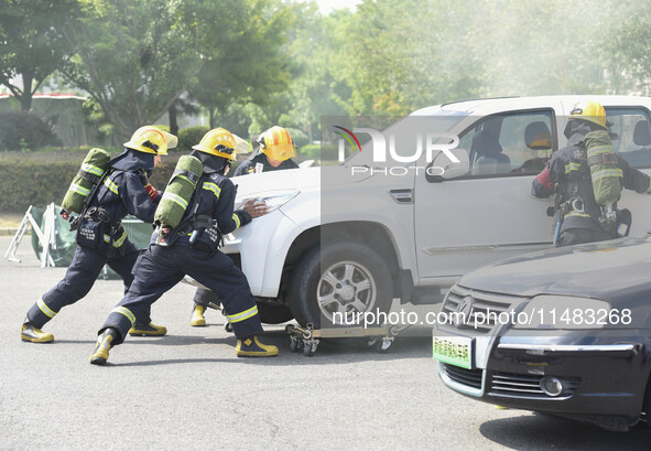 A firefighting robot is spraying water under the chassis of an electric vehicle that is simulated to be on fire and is lifting the vehicle t...