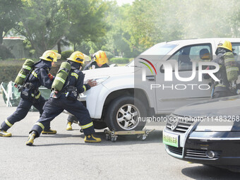 A firefighting robot is spraying water under the chassis of an electric vehicle that is simulated to be on fire and is lifting the vehicle t...