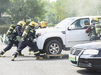 A firefighting robot is spraying water under the chassis of an electric vehicle that is simulated to be on fire and is lifting the vehicle t...