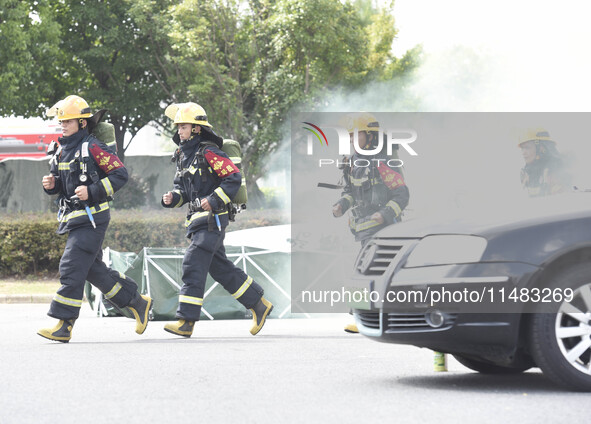 A firefighting robot is spraying water under the chassis of an electric vehicle that is simulated to be on fire and is lifting the vehicle t...