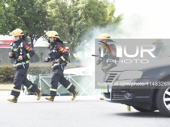 A firefighting robot is spraying water under the chassis of an electric vehicle that is simulated to be on fire and is lifting the vehicle t...