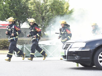 A firefighting robot is spraying water under the chassis of an electric vehicle that is simulated to be on fire and is lifting the vehicle t...