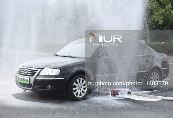 A firefighting robot is spraying water under the chassis of an electric vehicle that is simulated to be on fire and is lifting the vehicle t...