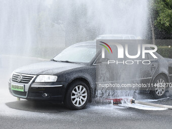 A firefighting robot is spraying water under the chassis of an electric vehicle that is simulated to be on fire and is lifting the vehicle t...