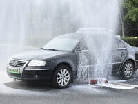 A firefighting robot is spraying water under the chassis of an electric vehicle that is simulated to be on fire and is lifting the vehicle t...