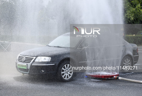 A firefighting robot is spraying water under the chassis of an electric vehicle that is simulated to be on fire and is lifting the vehicle t...