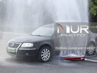 A firefighting robot is spraying water under the chassis of an electric vehicle that is simulated to be on fire and is lifting the vehicle t...