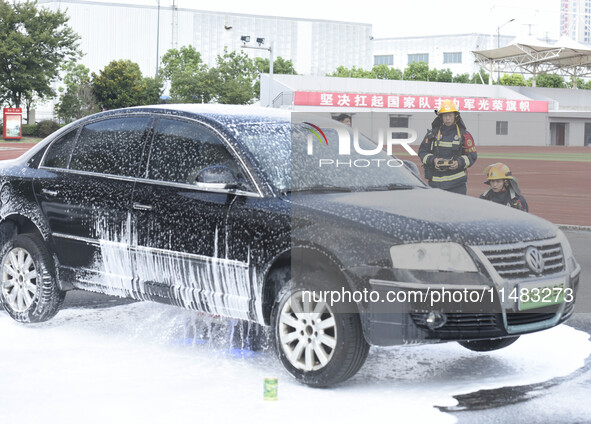 A firefighting robot is spraying water under the chassis of an electric vehicle that is simulated to be on fire and is lifting the vehicle t...