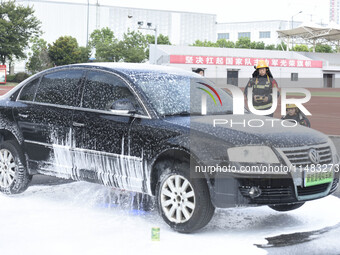 A firefighting robot is spraying water under the chassis of an electric vehicle that is simulated to be on fire and is lifting the vehicle t...