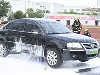 A firefighting robot is spraying water under the chassis of an electric vehicle that is simulated to be on fire and is lifting the vehicle t...