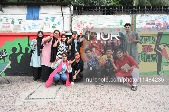 Students are showing their painted hands while painting graffiti on a wall alongside a road to express their message after the fall of Bangl...