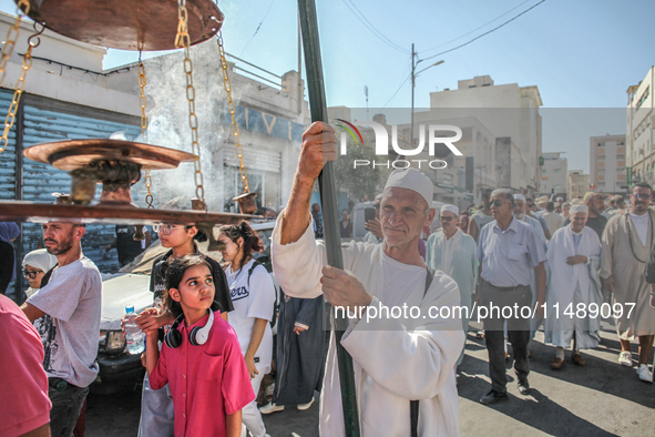 A devotee from a Sufi order in traditional Tunisian dress is carrying a Sufi flag with burning incense as he is leading the annual processio...