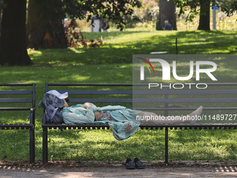 A person is taking an afternoon nap on a park bench at Queens Park in Toronto, Ontario, Canada, on August 14, 2024. (